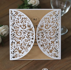 Detail of laser-cut lace wedding invitation on wood table with floral background