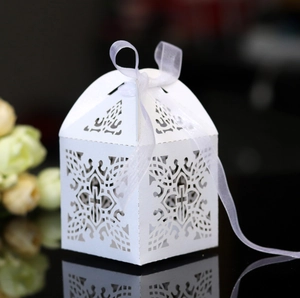 Macro shot of laser-cut white wedding candy box with cross pattern and organza ribbon