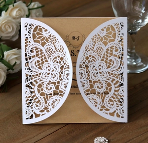 Close-up of laser cut lace wedding invitation with kraft paper insert on wooden background