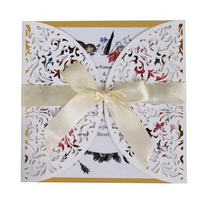 Elegant white laser-cut floral invitation card with a silk cream bow and golden accents