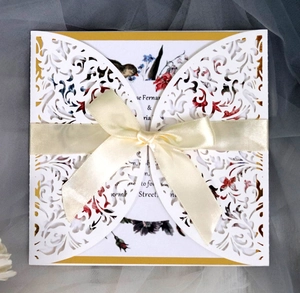 Detail of laser cut white invitation cover with golden lining and beige satin ribbon bow