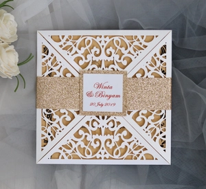Macro view of white laser-cut wedding invitation with gold glitter band and floral accents