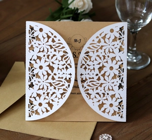 Detail of laser-cut floral wedding invitation with kraft insert on dark wood