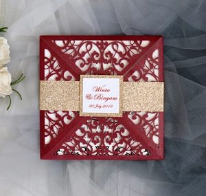 Detailed laser-cut pattern on red wedding invitation with gold glitter band and floral lace