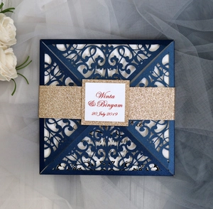 Close-up of laser-cut navy blue wedding invitation with gold glitter band and white floral decor