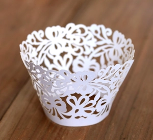Close-up of white laser-cut cupcake wrappers with intricate floral lace patterns on wood