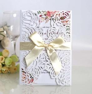 Close-up of laser-cut floral wedding invitation with cream ribbon and elegant insert card