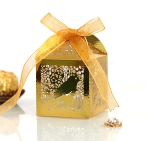 Macro view of golden laser-cut candy box with bird patterns and an orange ribbon bow