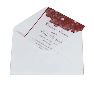 Elegant laser-cut white wedding invitation with deep red floral pattern and matching envelope