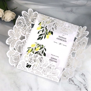 Laser-cut white floral wedding invitation with lemon pattern card on marble surface