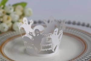 Detail of laser-cut white ghost and bat cupcake wrappers on a decorative ceramic plate