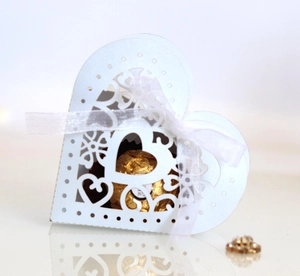 Detailed close-up of white laser-cut heart favor box with chiffon ribbon and chocolate inside