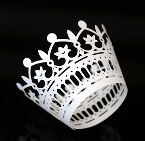 Detail of white laser-cut cupcake wrapper with a crown design on a dark background