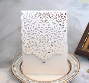 Detail of laser cut white rose wedding invitation with elegant teardrop pendant on ceramic plate