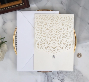 Close-up of laser-cut rose floral invitation cover with drop-shaped crystal on white marble