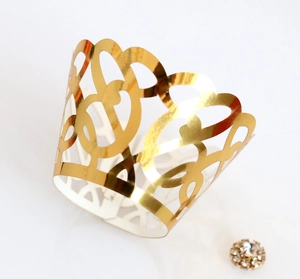Detail of laser-cut gold cupcake wrapper with heart and lace patterns on white background