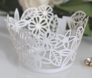 Detail of white laser-cut lace cupcake wrapper with intricate floral and leaf patterns