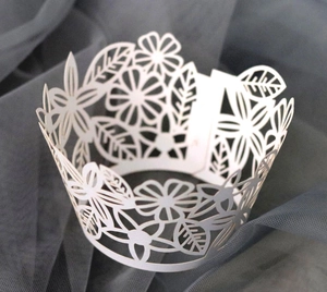 Close-up of white laser-cut cupcake wrappers with delicate floral and leaf patterns