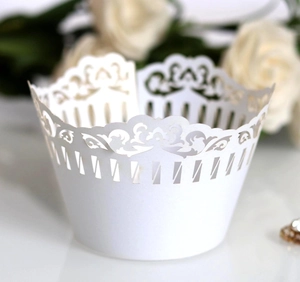 Close-up of white laser-cut cupcake wrappers with elegant lace vine pattern and vertical stripes