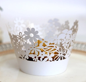 Close-up of white laser-cut cupcake wrapper with daisy floral pattern on a porcelain plate