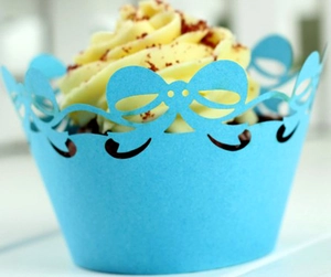 Close-up of laser-cut blue cupcake wrappers with bow-knot lace and scallop edge pattern