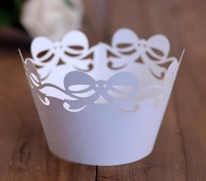 Macro shot of white laser-cut cupcake wrappers featuring elegant lace bow patterns