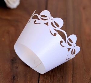 Macro shot of laser-cut white lace cupcake wrappers with bow design on dark wood