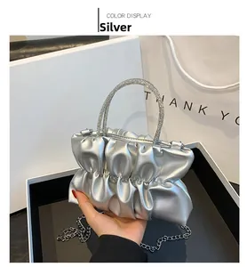 Detail van zilveren geplooide cloud bag met fonkelend strass handvat en fijne metalen ketting