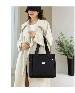Detail of black nylon tote bag featuring a silver logo plate and multiple exterior pockets
