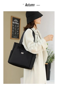 Detail view of large black oxford tote bag with side pocket and silver metal nameplate