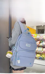 Detail of light blue nylon backpack with multi-pockets, cute plush charms and embroidery