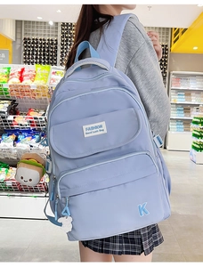 Detail of light blue waterproof backpack with multiple zippers and plush burger charm accessory