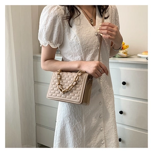 Detailed view of beige quilted crossbody bag with textured squares and chain handle