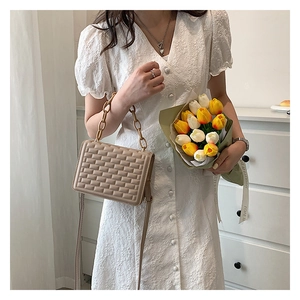 Detail of beige quilted shoulder bag with chain strap held by model with tulips