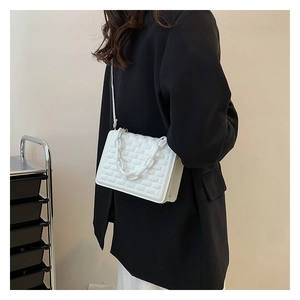White quilted crossbody bag with chunky chain detail worn by a model in a black suit