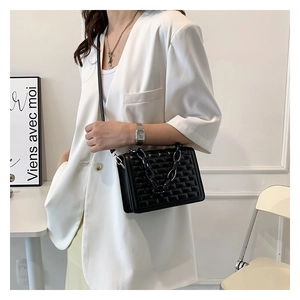 Detail of black geometric quilted crossbody bag with stylish chunky chain on white blazer