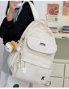 Detail of cream multi-pocket backpack with plush burger charm and fashion embroidery