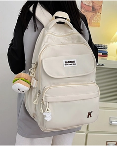 Detail view of off-white waterproof backpack with multiple pockets and cute burger charm