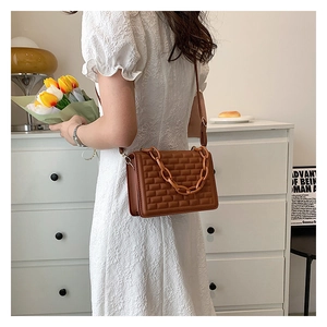 Close-up of brown quilted shoulder bag with chain strap detail on a lifestyle background