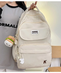 Detail view of cream waterproof nylon backpack featuring cute burger plush charms and embroidery
