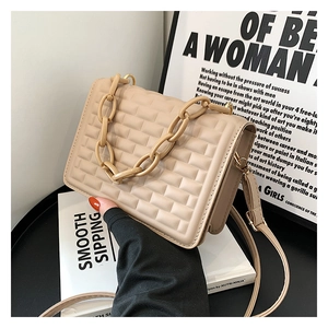 Close-up of beige quilted crossbody bag with chunky chain handle and embossed texture