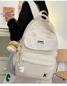 Detail view of cream nylon backpack with plush charms and embroidered K letter