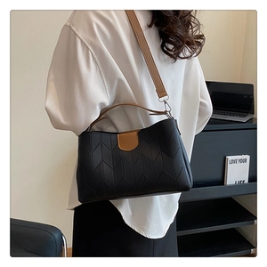 Detail of black chevron quilted leather handbag with brown strap shown in office setting