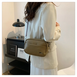 Detail shot of khaki lychee grain crossbody bag with metal logo and textured leather finish