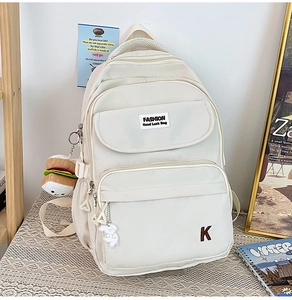 Detail view of water-resistant beige backpack with cute charms and front zipper pockets