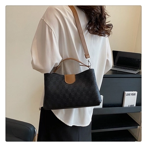 Detail view of black geometric embossed handbag with brown leather straps on model