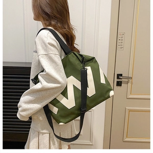 Detail of dark green canvas tote bag with large white W letter worn as a crossbody bag