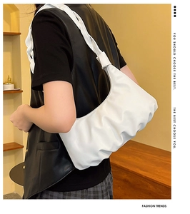 Detailed close-up of a white pleated dumpling bag with glossy finish and flat shoulder strap