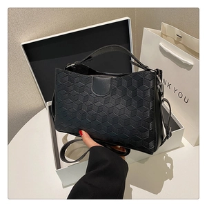 Close-up of black handbag with 3D geometric texture, gift box and white paper bag
