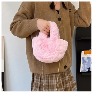 Rosa Plüsch-Handtasche mit goldener Kette an einem Modell für die Herbstmode präsentiert